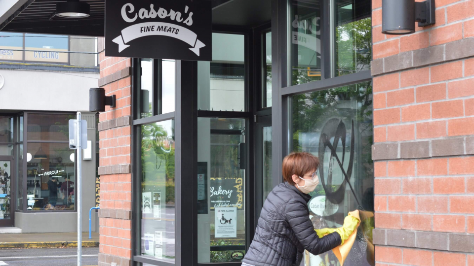 Sarah wearing gloves and a mask, cleaning spray paint off the front window of Cason's Fine Meats