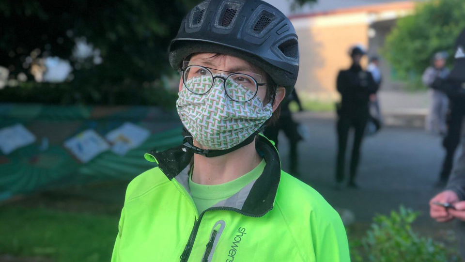 Sarah at a protest, wearing a mask, with police in the background
