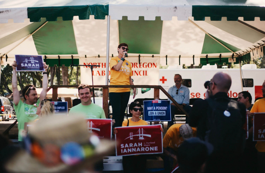 Sarah speaking to a crowd from a tented stage at her campaign kickoff event.